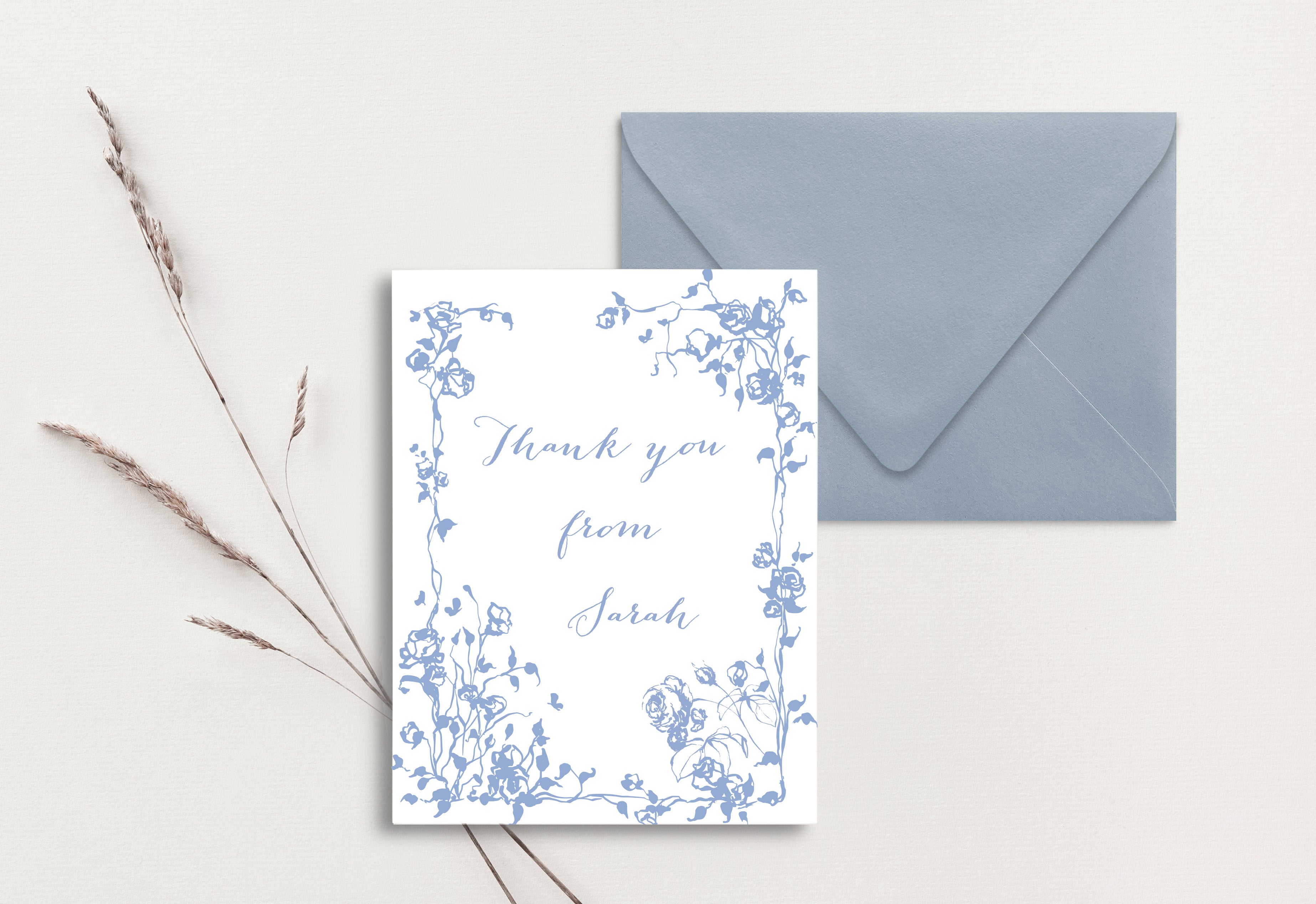 A custom thank you card with a blue floral print design, accompanied by a grey envelope, displayed on a white background with some dried plant stems to the side.