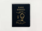 Black passport holder with gold text and hot air balloon design